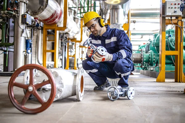 Hardworking industrial technician inspecting high pressure valve inside refinery plant.