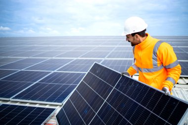 Fabrikanın çatısına ucuz sürdürülebilir enerji veya elektrik için güneş panelleri kuran endüstriyel işçiler.