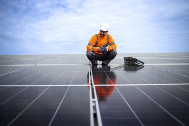 Solar energy plant worker installing additional photovoltaic panels on the factory roof.