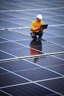 Dizüstü bilgisayarlı profesyonel işçi güneş enerjisi santralinin elektrik üretimini kontrol ediyor.