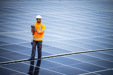 Professional worker with laptop computer controlling electricity production of solar power plant.