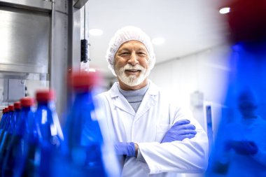 Portrait of an experienced man worker in white sterile coat standing in food and bottling factory.