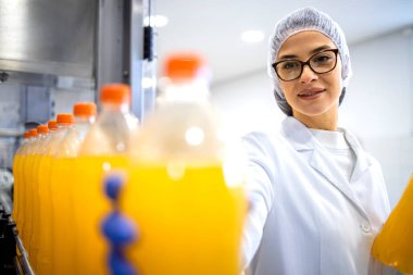 Bottling factory interior and female worker checking orange juice production. clipart