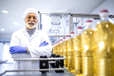 Portrait of food industry expert or technologist in white sterile uniform and standing by conveyor belt machine inside bottling plant.