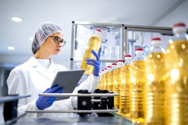 Food inspector or technologist doing quality control of bottled vegetable oil inside bottling plant. clipart