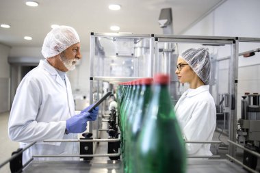 Quality control inspectors working inside bottling plant checking carbonated water production.