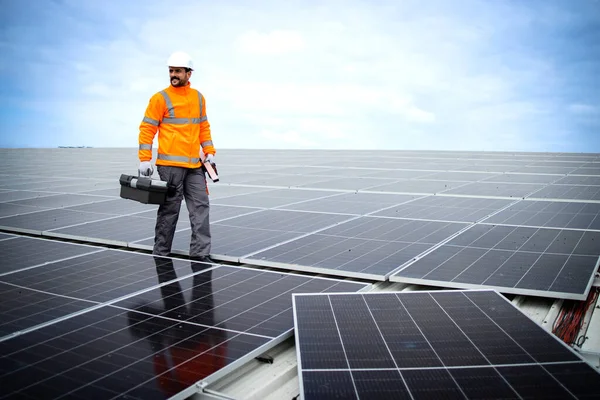 Professional worker in high visibility suit and hardhat mounting solar panels on the rooftop.