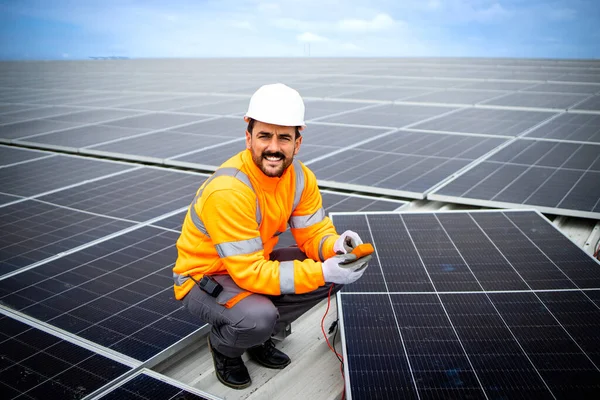 Solar energy industry worker standing on the rooftop holding electrical measuring device and checking panel installation.