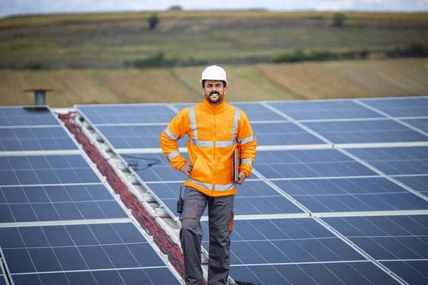 Portrait of industrial solar engineer worker proudly standing on the roof after successful installation of photovoltaic cell panels for electricity production.