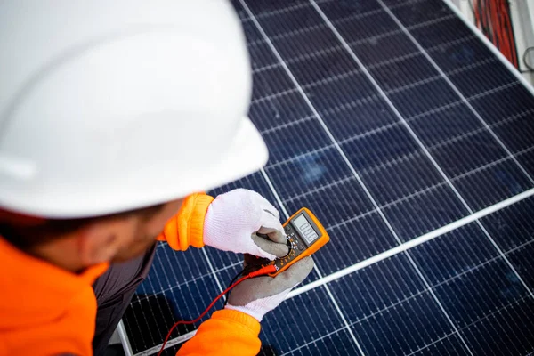 Solar energy worker checking voltage and electricity via multimeter of installed photovoltaic panels.
