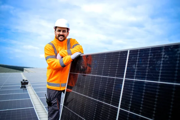 Portrait of solar energy worker holding photovoltaic panel and standing in solar power plant.