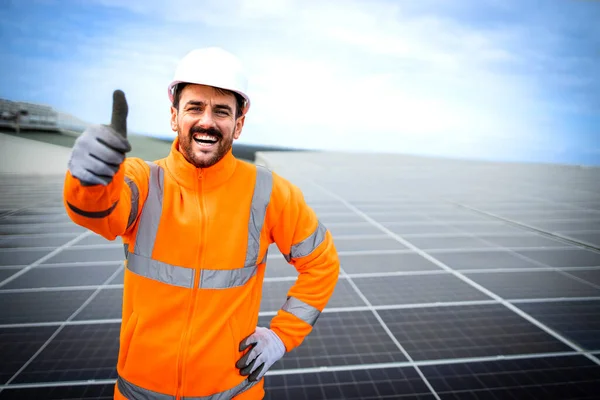 Portrait of solar energy worker with thumbs up standing in solar power plant.