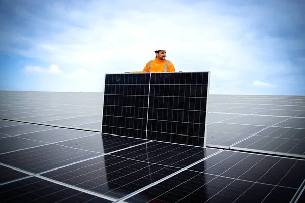 Professional worker in high visibility suit and hardhat mounting solar panels on the rooftop.