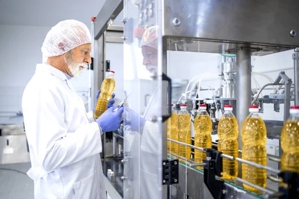 Food factory and experienced production line worker standing by industrial machine and controlling production of bottled vegetable oil.