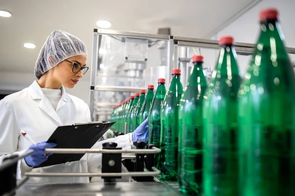 飲料水や包装の生産を管理する瓶詰め工場で働く女性技術者 — ストック写真