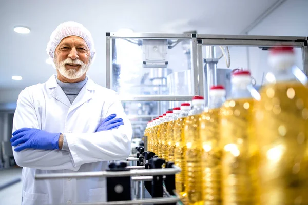 Portrait of food industry expert or technologist in white sterile uniform and standing by conveyor belt machine holding his arms crossed.