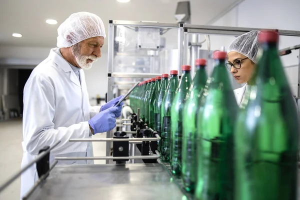 PET packaging bottling plant and workers in white coat controlling water production.