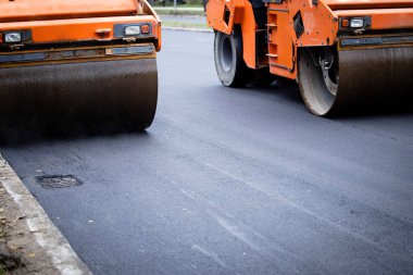 Road construction machinery in action and asphalt paving machine making new layer flat and smooth.