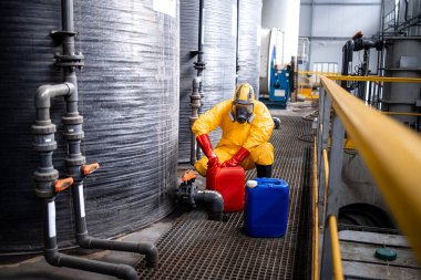 Professional worker in safety suit working with dangerous chemicals and acids in factory.