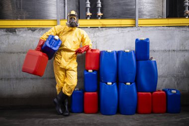 Portrait of professional worker in hazmat suit and gas mask standing inside chemicals factory and holding canisters. clipart