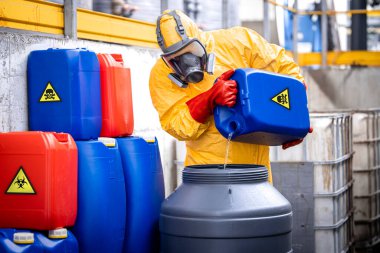Experienced factory worker in protection suit and gas mask mixing dangerous and poisonous chemicals inside production plant.