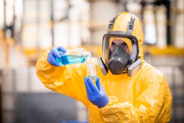 Quality control worker in protection suit and gas mask testing quality of chemical inside chemicals production factory .