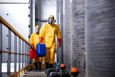 Sarı takım elbiseli, gaz maskeli ve eldivenli tam korumalı işçiler tehlikeli kimyasallar ve maddelerle uğraşıyorlar..