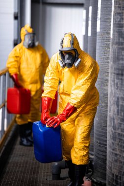 Fully protected workers in yellow hazmat suit, gas masks and gloves handling dangerous chemicals or substances.