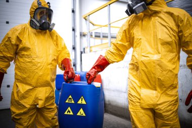 Chemicals production factory. Experienced workers fully protected in gas mask carrying hazardous and toxic waste in chemical plant.