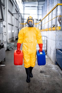 Portrait of factory worker wearing protective suit and gas mask carrying chemicals inside industrial production plant.