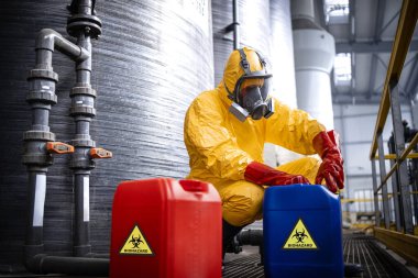 Chemicals industry production. Fully protected worker in yellow suit, gas mask, gloves and boots working with hazardous waste.