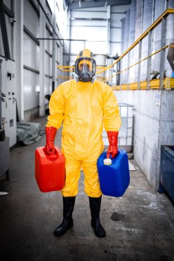 Portrait of factory worker wearing protective suit and gas mask carrying chemicals inside industrial production plant.
