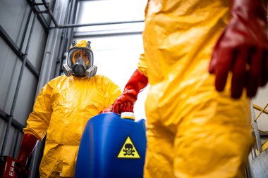 Working in chemicals warehouse. Workers fully protected against toxic fumes carrying dangerous materials.