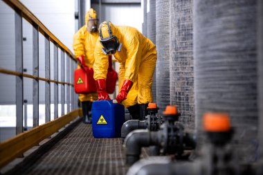 Experienced and trained workers with gas masks handling hazardous material inside chemicals factory.