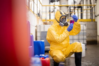 Quality control worker in protection suit and gas mask testing quality of chemical inside chemicals production factory .