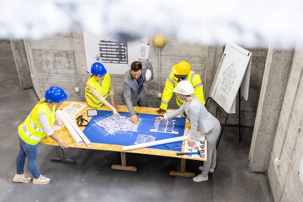 stock image Top view of contractor and architects analyzing plans and blueprints of the new project at construction site.