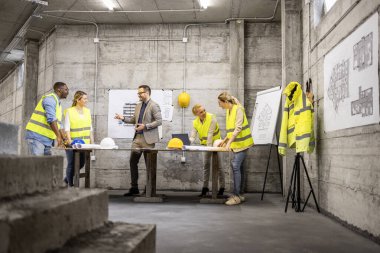 İnşaat alanındaki yeni projenin planlarını ve planlarını inceleyen müteahhit ve mimarlar.