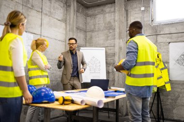 Yapı mühendisleri ve mimarlardan oluşan bir ekip inşaat sahasında yapı tesisi veya planlarını analiz etmek için bir toplantı yapıyor..