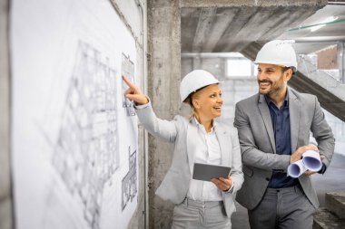 İnşaat mühendisleri inşaat alanında birlikte çalışıp inşaat sürecini kontrol ediyorlar. Proje planına ve planına bakıyorum..