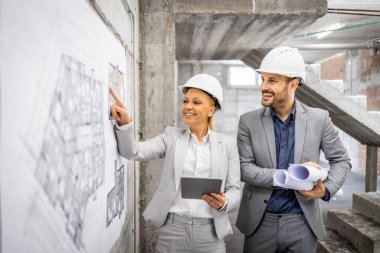 İnşaat mühendisleri inşaat alanında birlikte çalışıp inşaat sürecini kontrol ediyorlar. Proje planına ve planına bakıyorum..