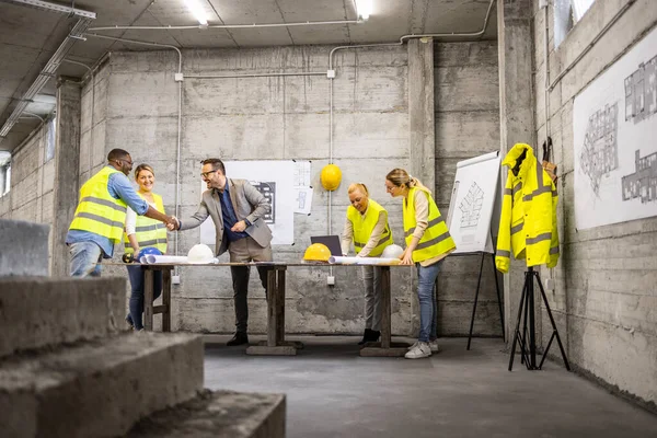 stock image Team of structural engineers and architects analyzing plans and blueprints at construction site.