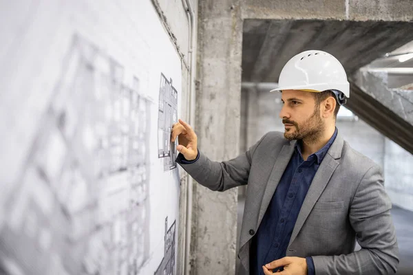 stock image Focused caucasian construction engineer checking blueprints and project plan at building site.