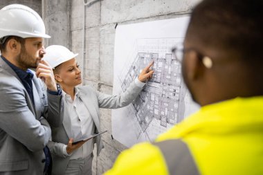 İnşaat işçisi ve mimarlar inşaat sahasında proje planı ve inşaatın bir sonraki aşamasını analiz ediyorlar..
