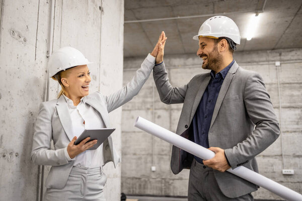 Architect giving high - five to construction engineer for successful cooperation.