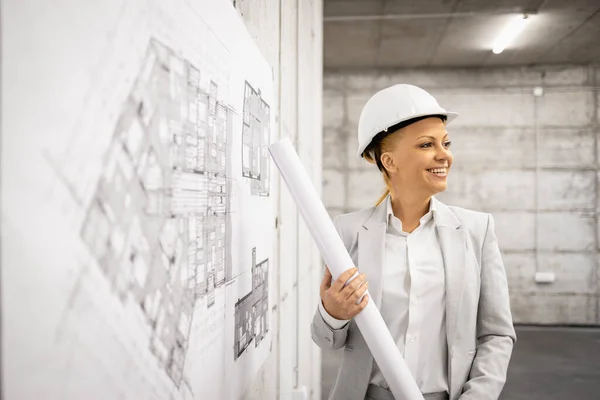 stock image Beautiful smart female civil engineer holding blueprints at construction site.