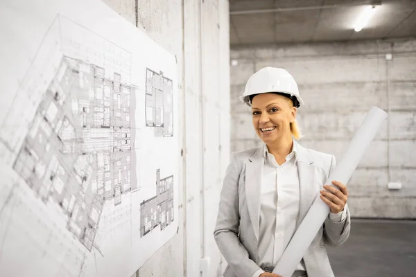 stock image Beautiful smart female civil engineer holding blueprints at construction site.