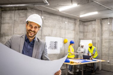 İş elbisesi içindeki gülümseyen yapı mühendisinin portresi ve inşaat planının bulunduğu yerde..