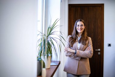 Ofisin penceresinde kollarını kavuşturmuş çekici bir iş kadınının portresi..