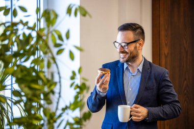 İş adamı çörek yiyor ve iş yerinde kahve içiyor..