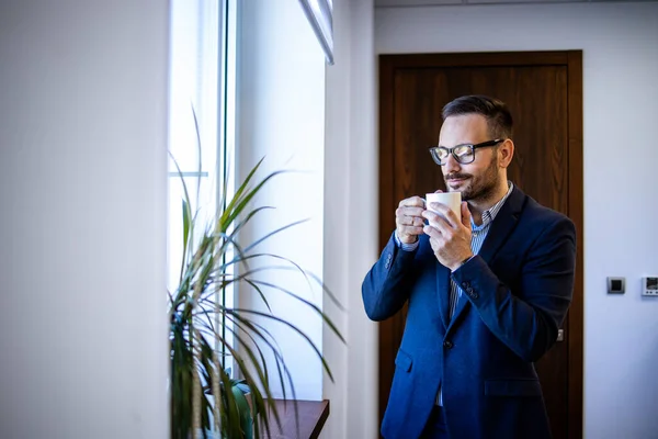 stock image Portrait of successful manager or director standing in his office, drinking coffee and looking through the window.